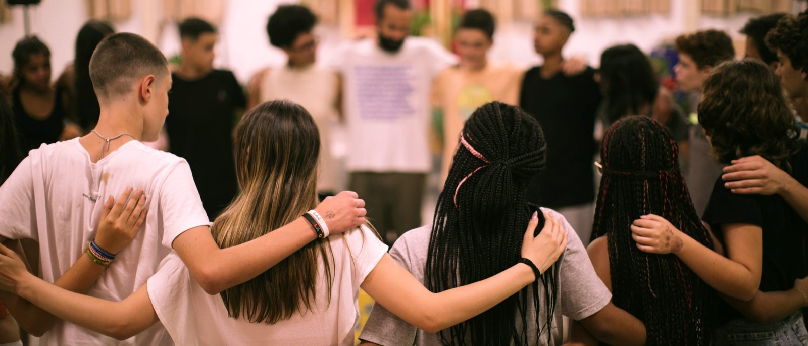 Roda de adolescentes abraçados pelos ombros, de costas para a câmera.