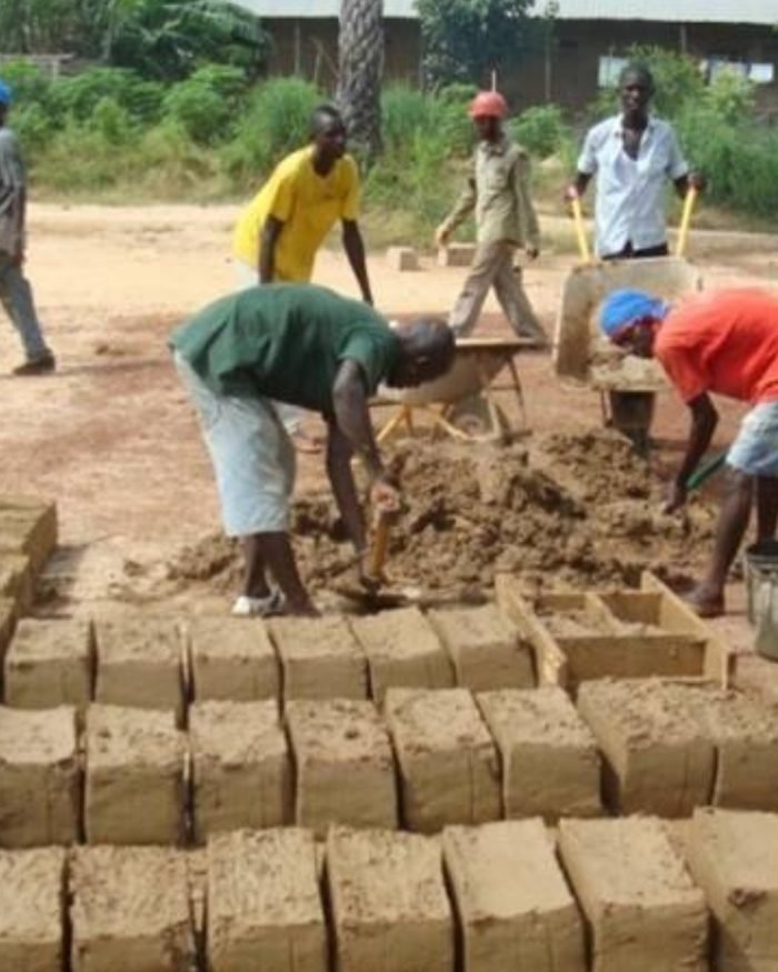 Homens moldando tijolos de adobe em fileiras no chão, durante o mutirão de construção.