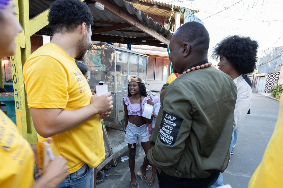 Pessoas de camiseta amarela conversando com moradores numa passagem da comunidade.