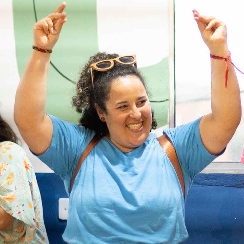 Priscilla Pereira de braços erguidos, sorrindo, com óculos de sol na cabeça.