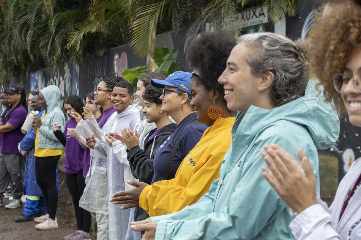 Fila de pessoas aplaudindo, lado a lado, durante uma atividade ao ar livre.