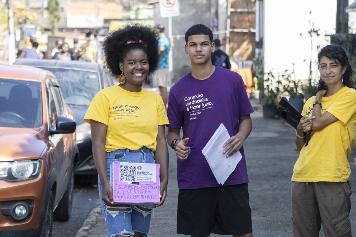 Dois jovens com pranchetas numa rua, anotando durante a escuta com moradores.