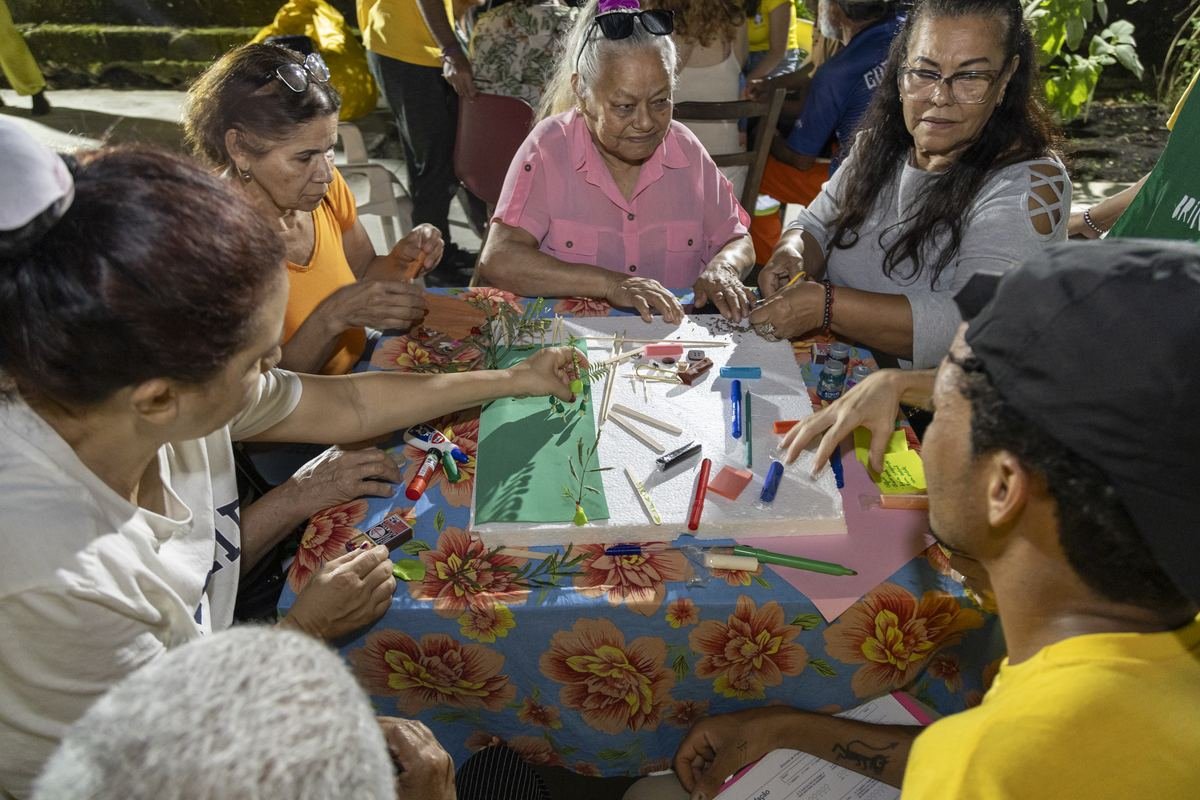 Roda de trabalho ao ar livre: pessoas sentadas em círculo, conversando sobre folhas de papel espalhadas no chão.
