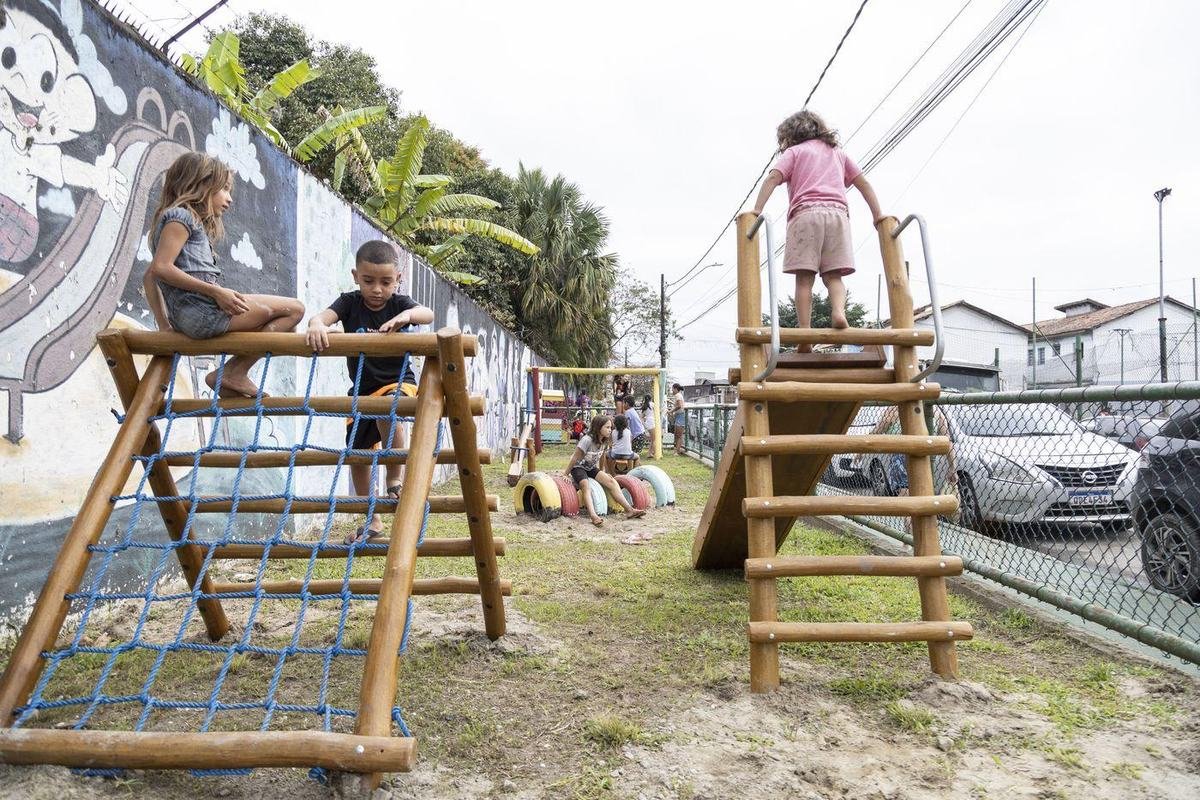 Crianças brincando no trepa-trepa de madeira do parquinho novo.