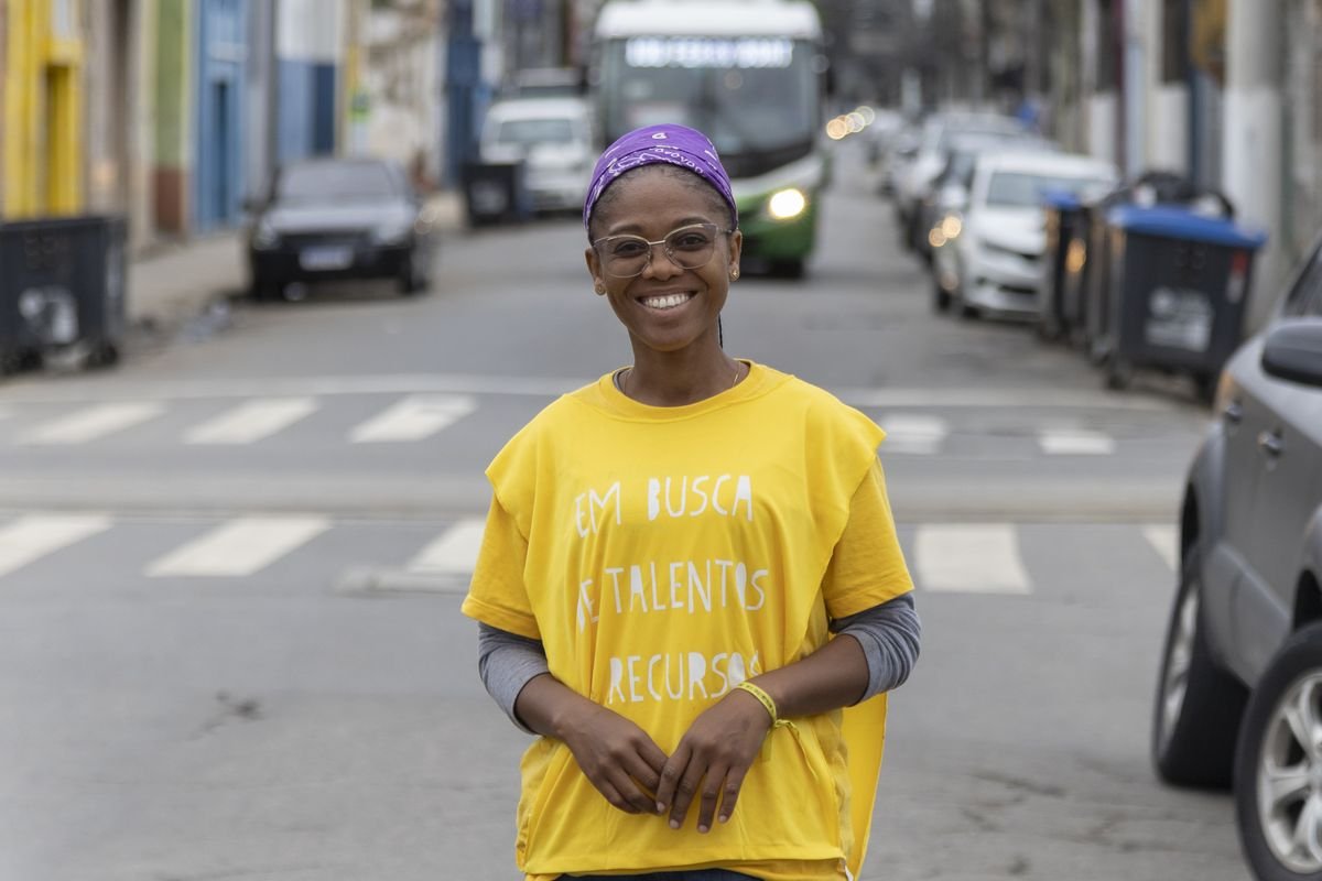 Jovem de camiseta amarela sorrindo no meio da rua.