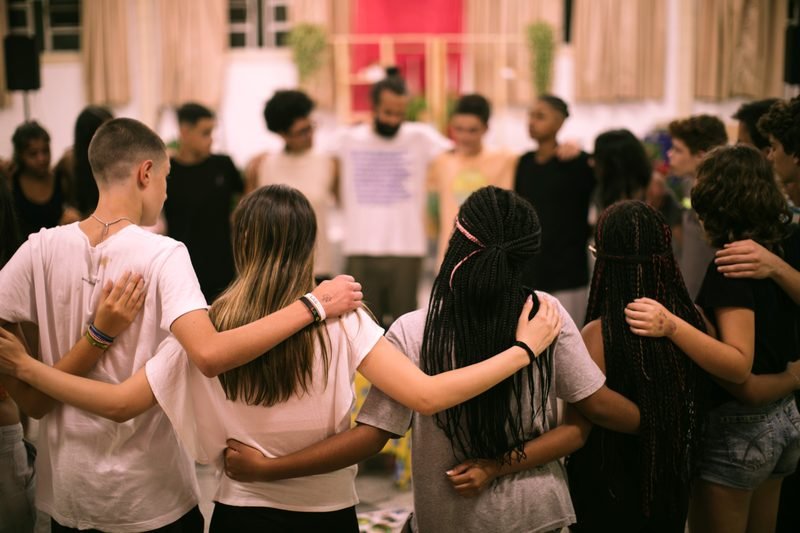 Roda de adolescentes abraçados pelos ombros, de costas para a câmera.
