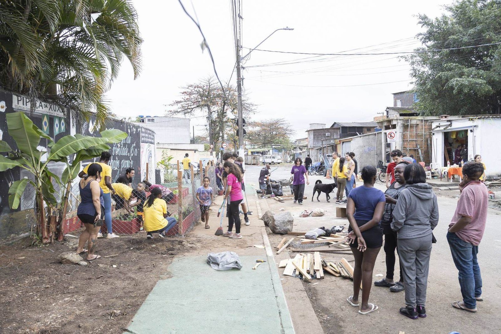 Rua de comunidade durante o mutirão, com gente trabalhando ao longo do quarteirão inteiro.